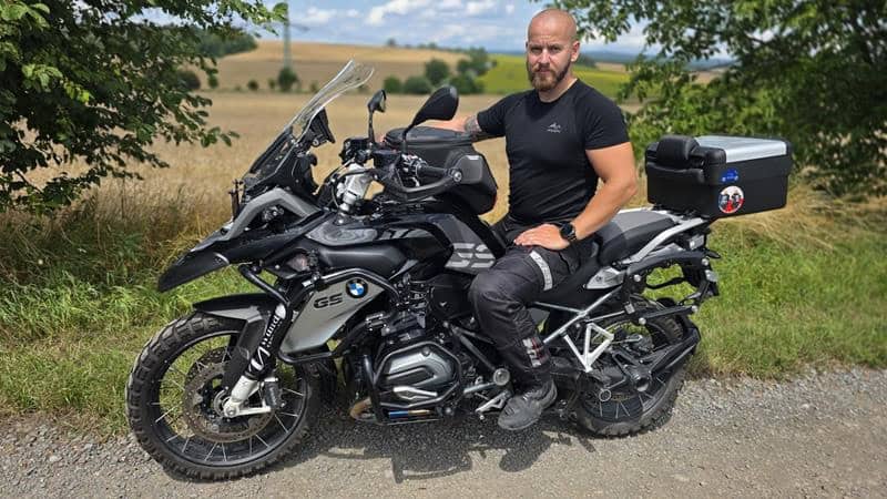 На снимката е мъж, седнал на модерна моторка BMW GS в природна среда.