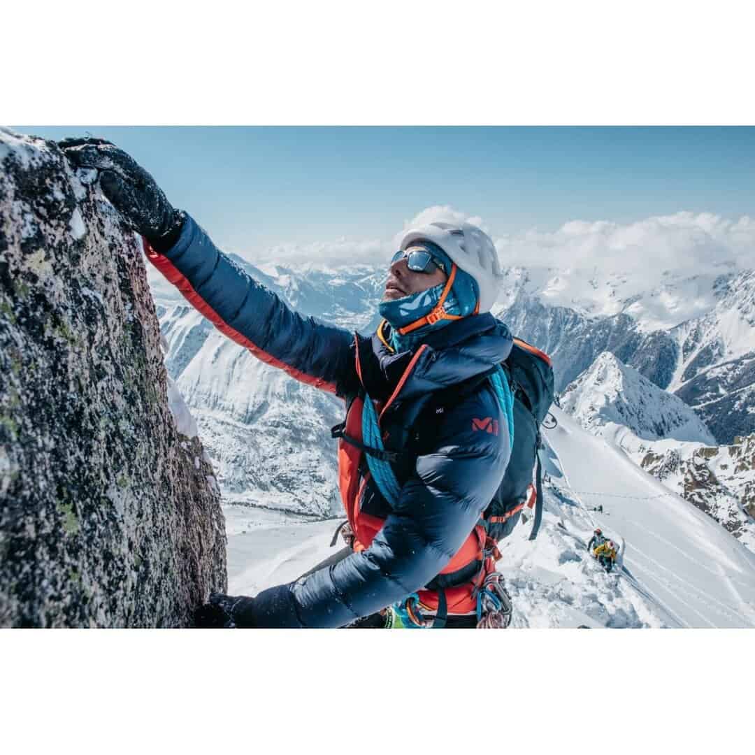 Мъж, катерещ се по скала в снежна планина, зимен спорт.