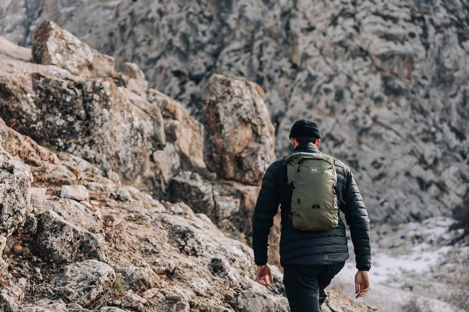 Мъж с раница, изкачващ се по скалист път в планината.