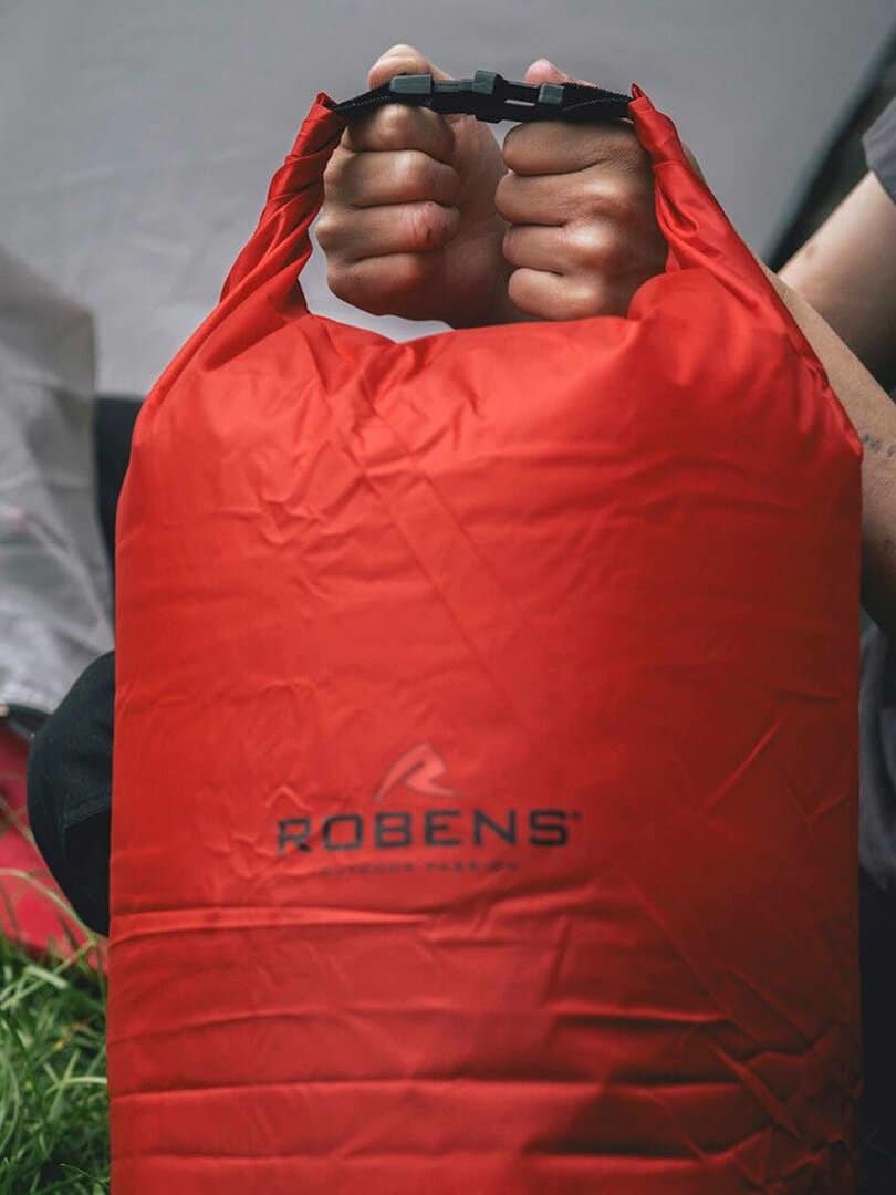 Човек държи червена водоустойчива раница Robens с дръжка.