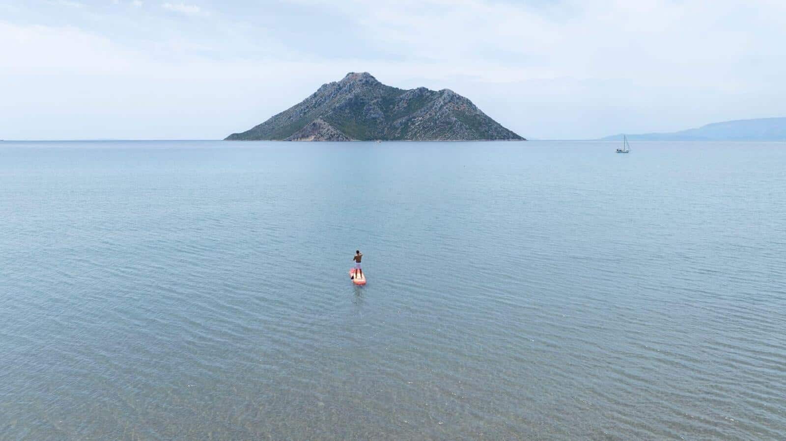 Почиващ на SUP на спокойна вода с остров на заден план.