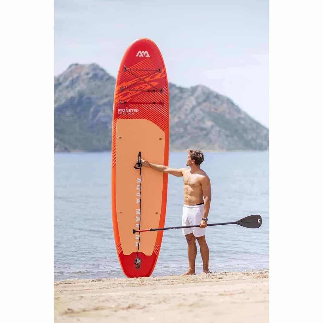 Мъж с SUP Aqua Marina Monster 12 на плажа, планини на заден план.