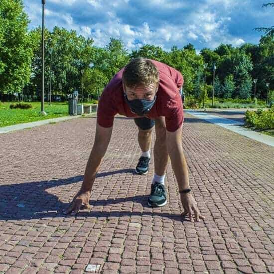 Мъж с маска в стартова позиция на пътеката в парка.
