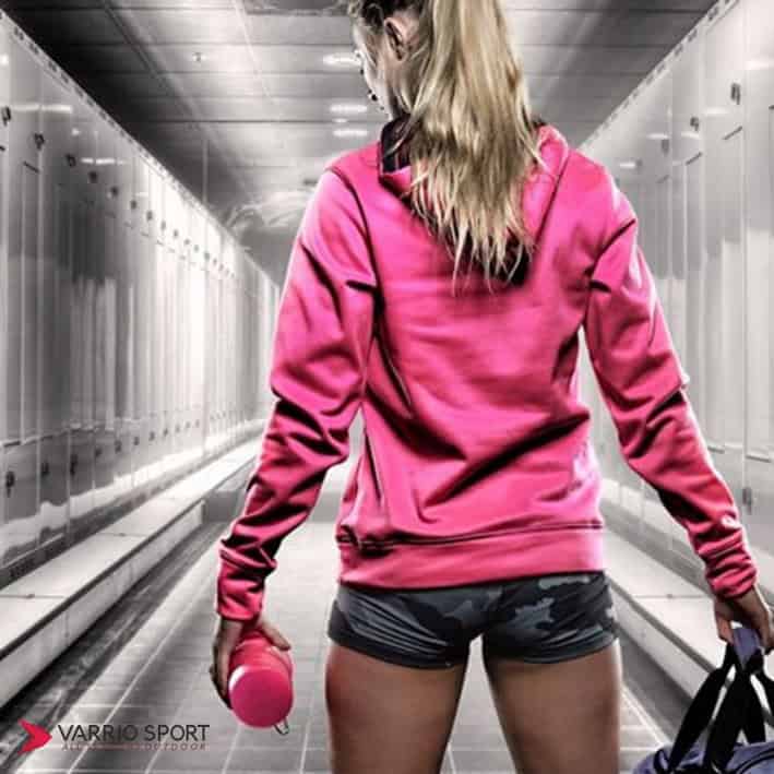 Жена с розова спортна блуза и бутилка в спортна зала.