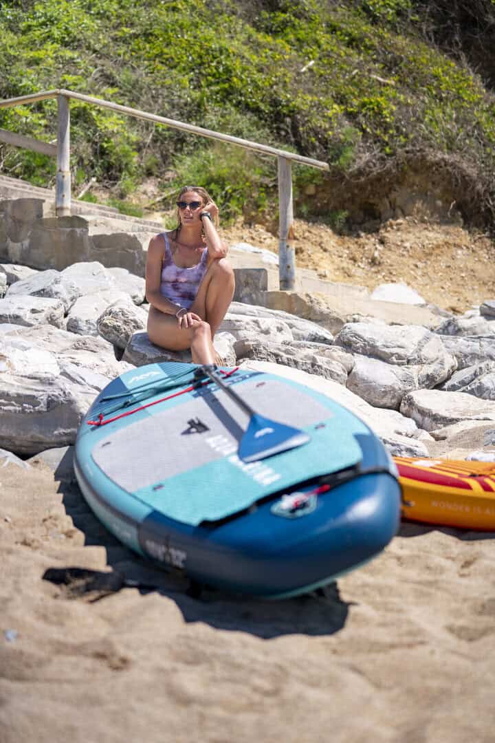 Жена с SUP на плажа, готова за водни спортове, слънчево време.